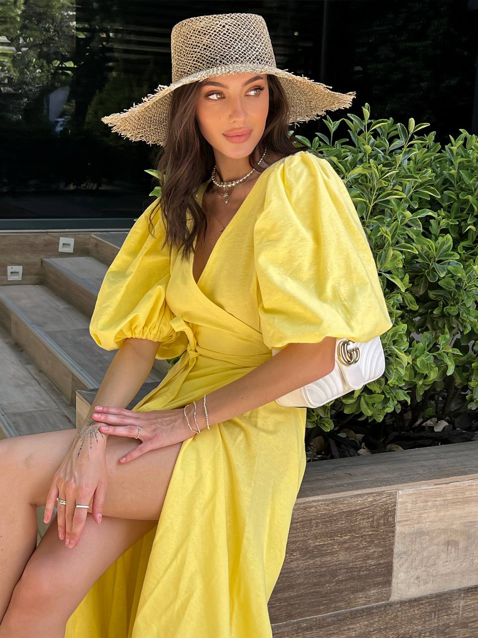 Woman in a yellow dress and straw hat sitting outdoors.