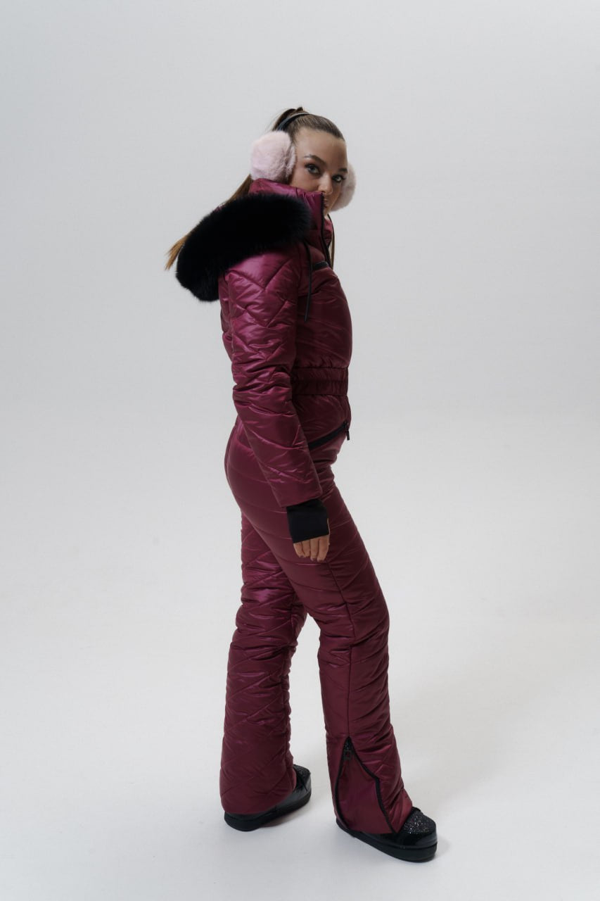 Person wearing a maroon snowsuit with black earmuffs on a white background