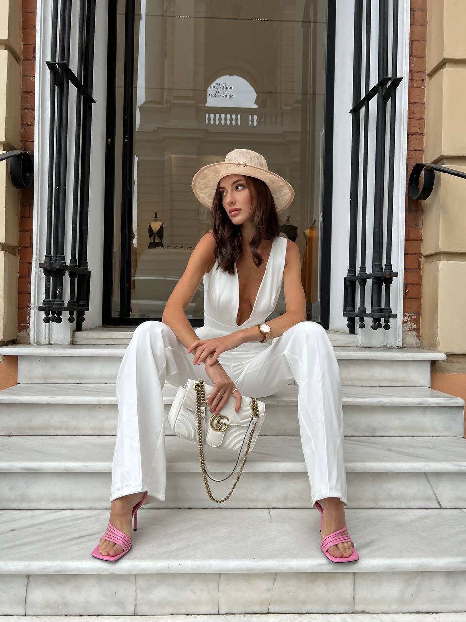 Woman in a white outfit sitting on steps wearing a straw hat.