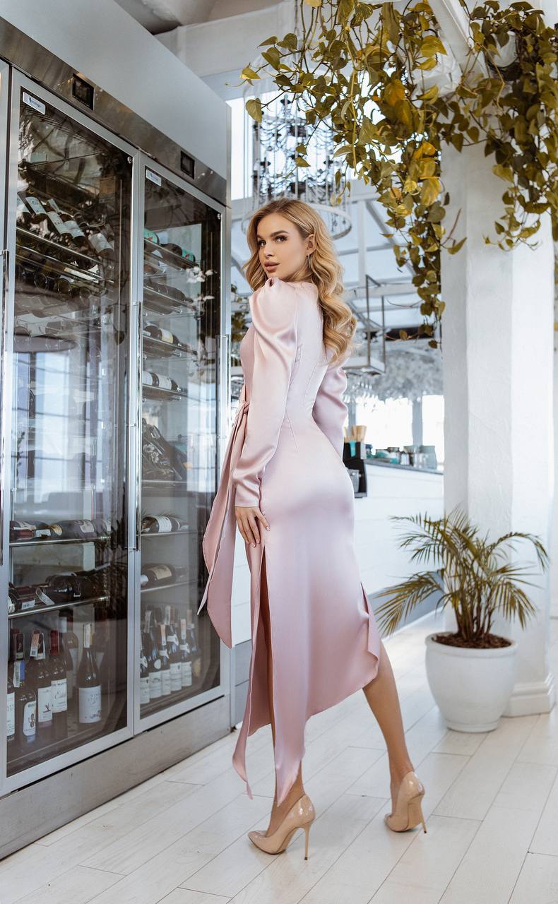Woman in a pink dress standing in a modern interior setting with glass doors and decorative plants.