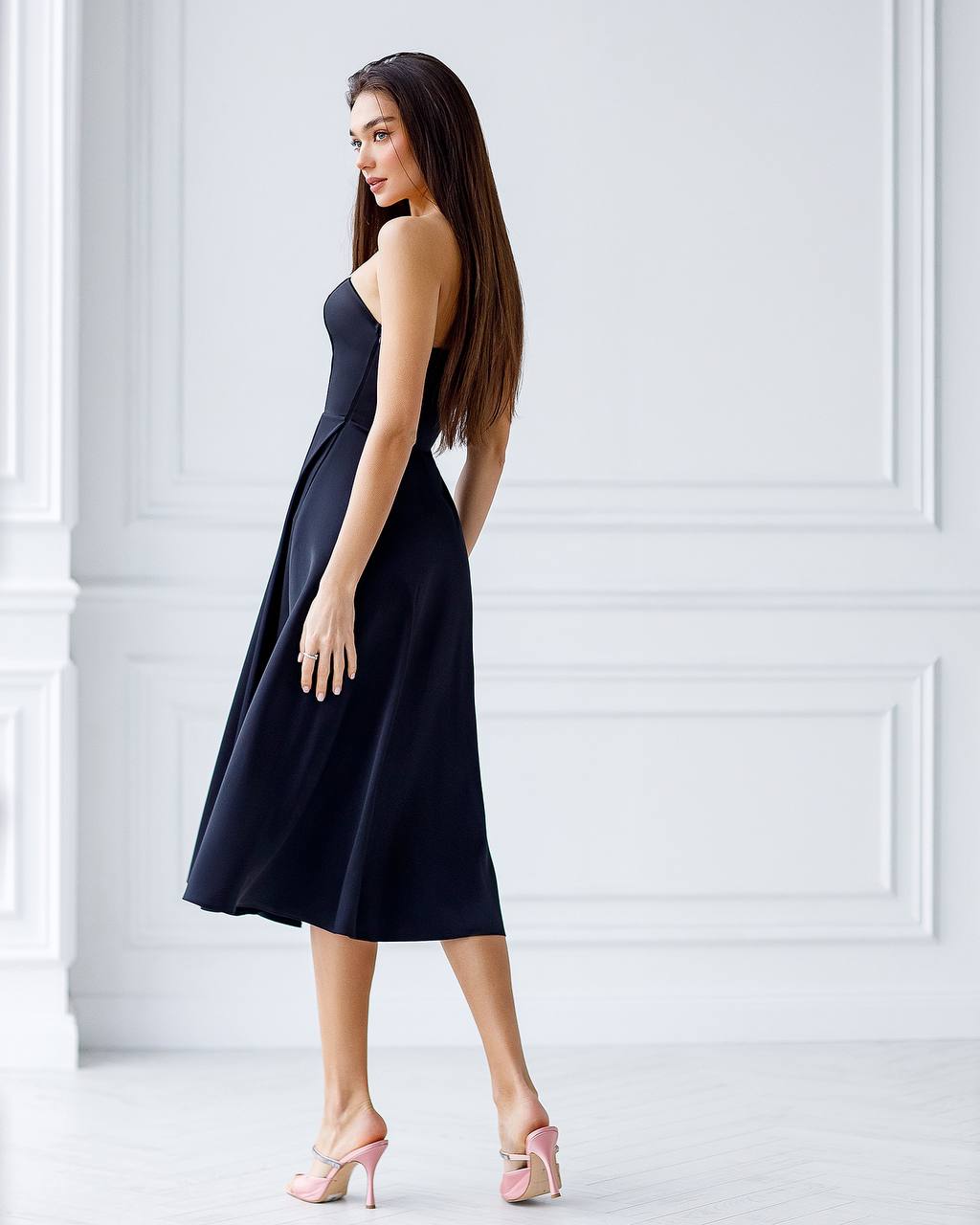 Woman wearing a black dress with pink shoes against a white wall