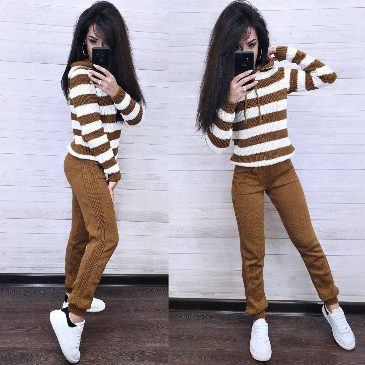 Woman wearing a brown and white striped sweater and brown pants, taking a mirror selfie.