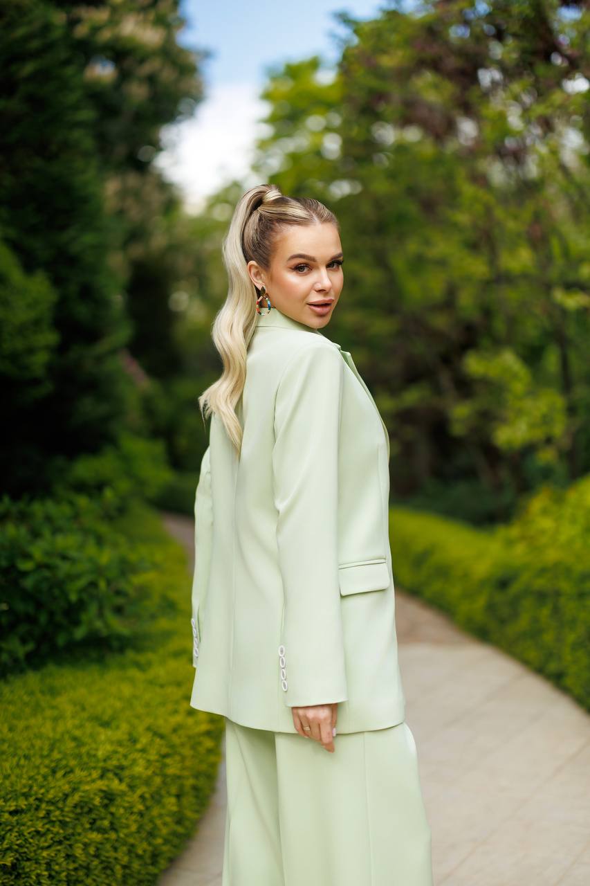 Woman in a light green outfit standing on a path with greenery around