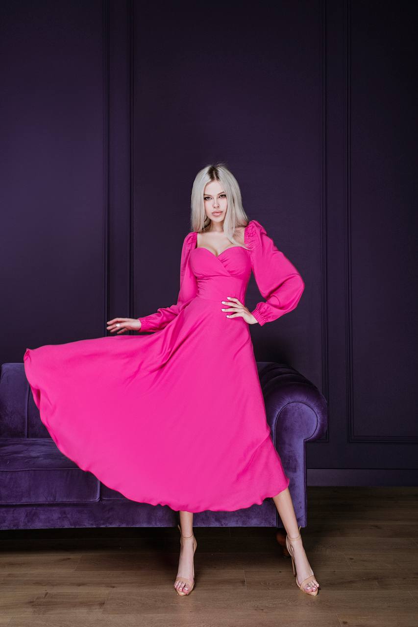 Woman in a pink dress posing in a room with purple walls and furniture.