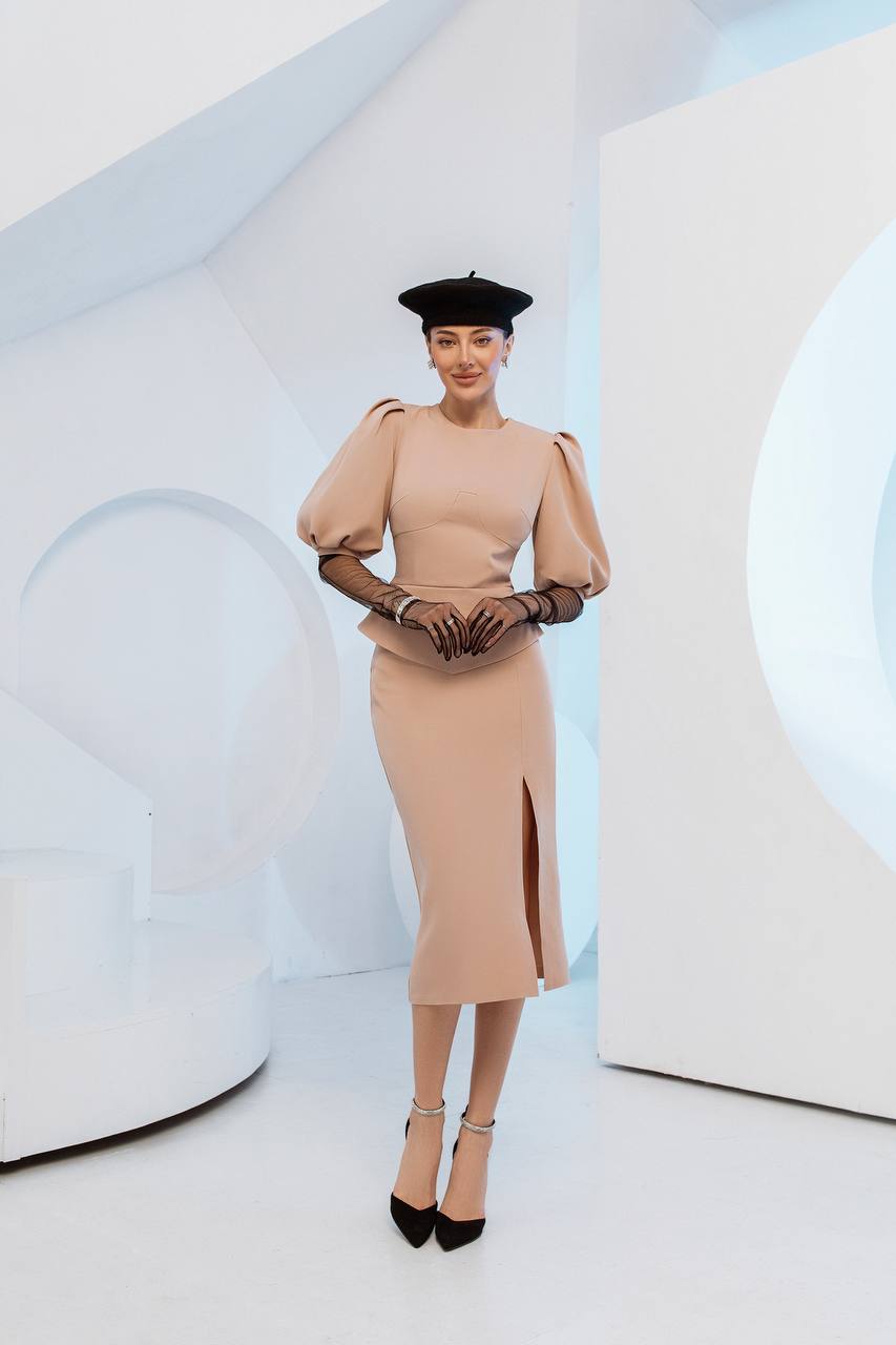 Woman in a beige dress with puffed sleeves and a black hat against a white background