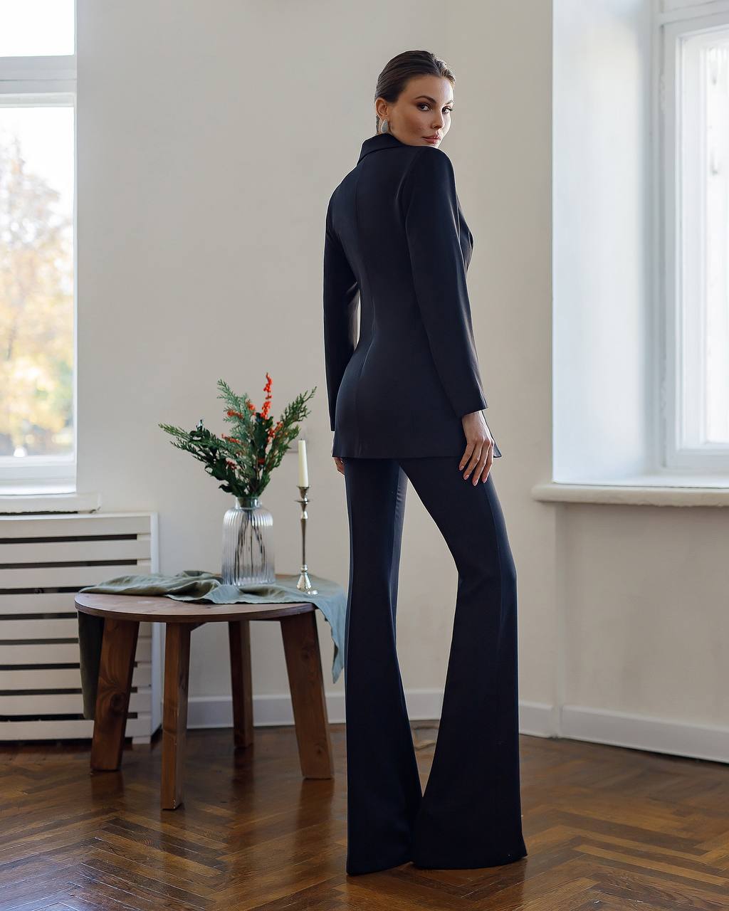 Woman in a navy blue suit standing in a room with a small table and decorative items.