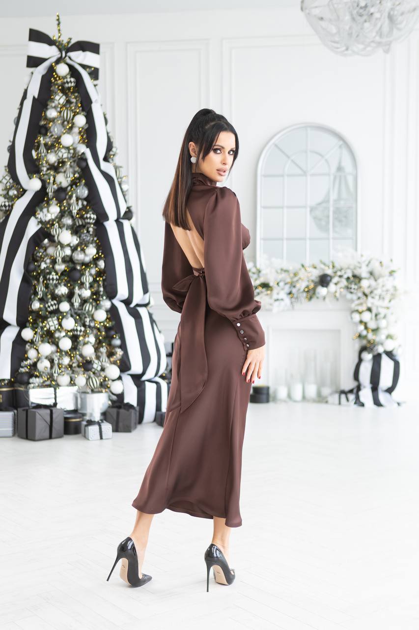 Woman in a brown dress standing in a decorated room with a Christmas tree and floral arrangements.