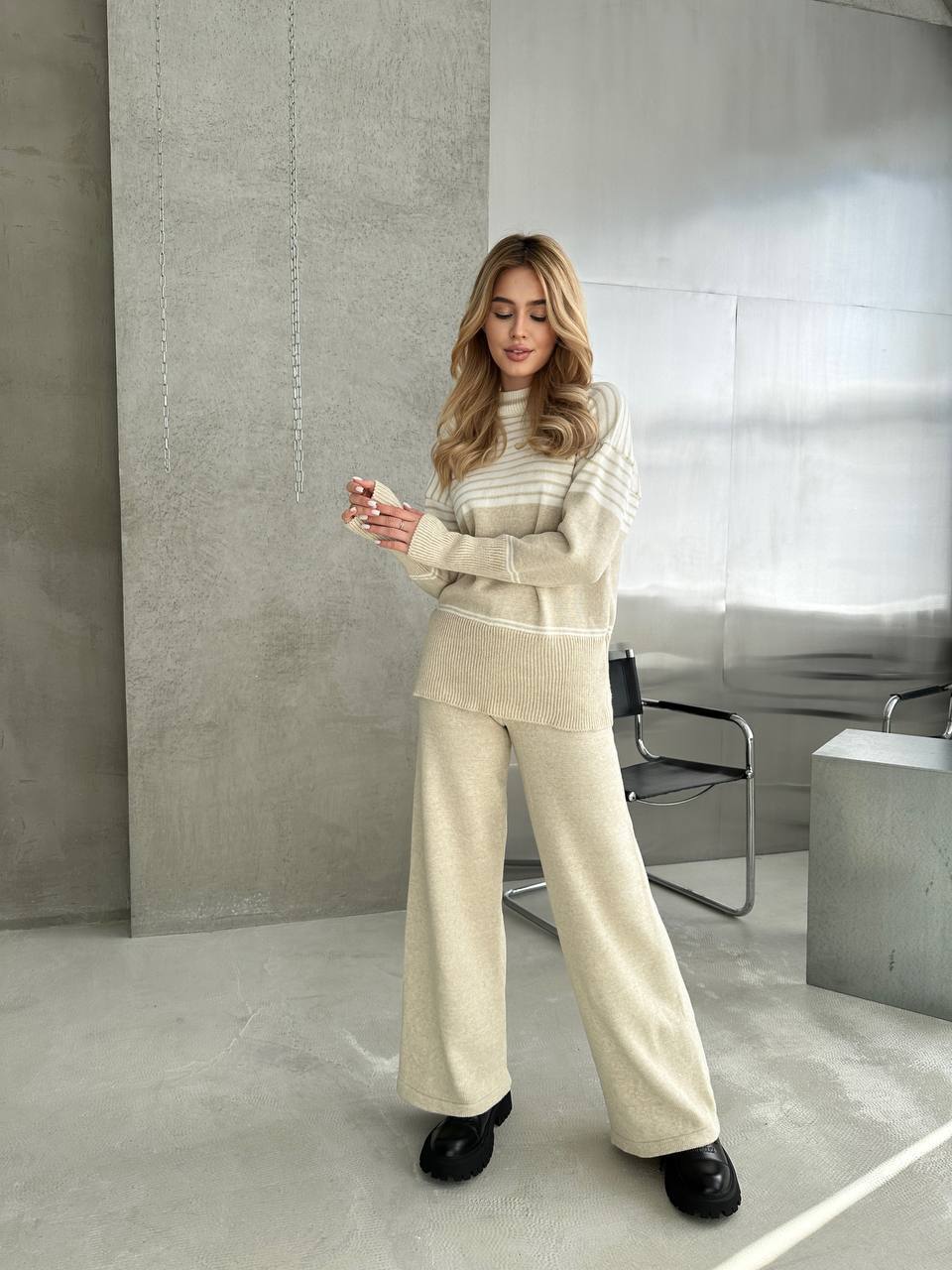 Woman in a beige outfit standing in a modern room with concrete walls and floor.