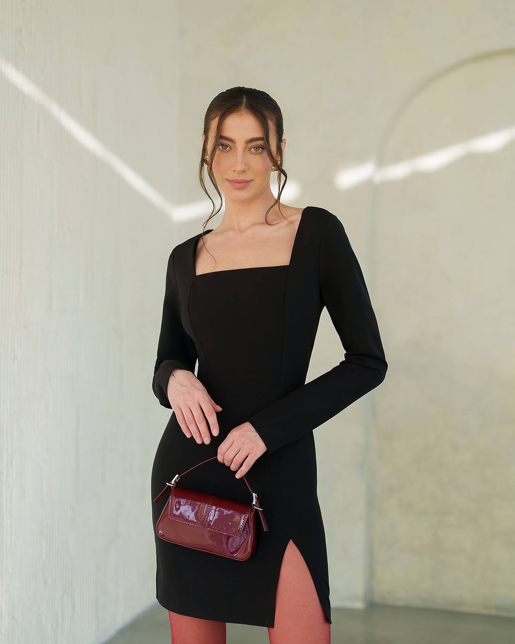 Woman wearing a black dress holding a red handbag in a minimalistic setting
