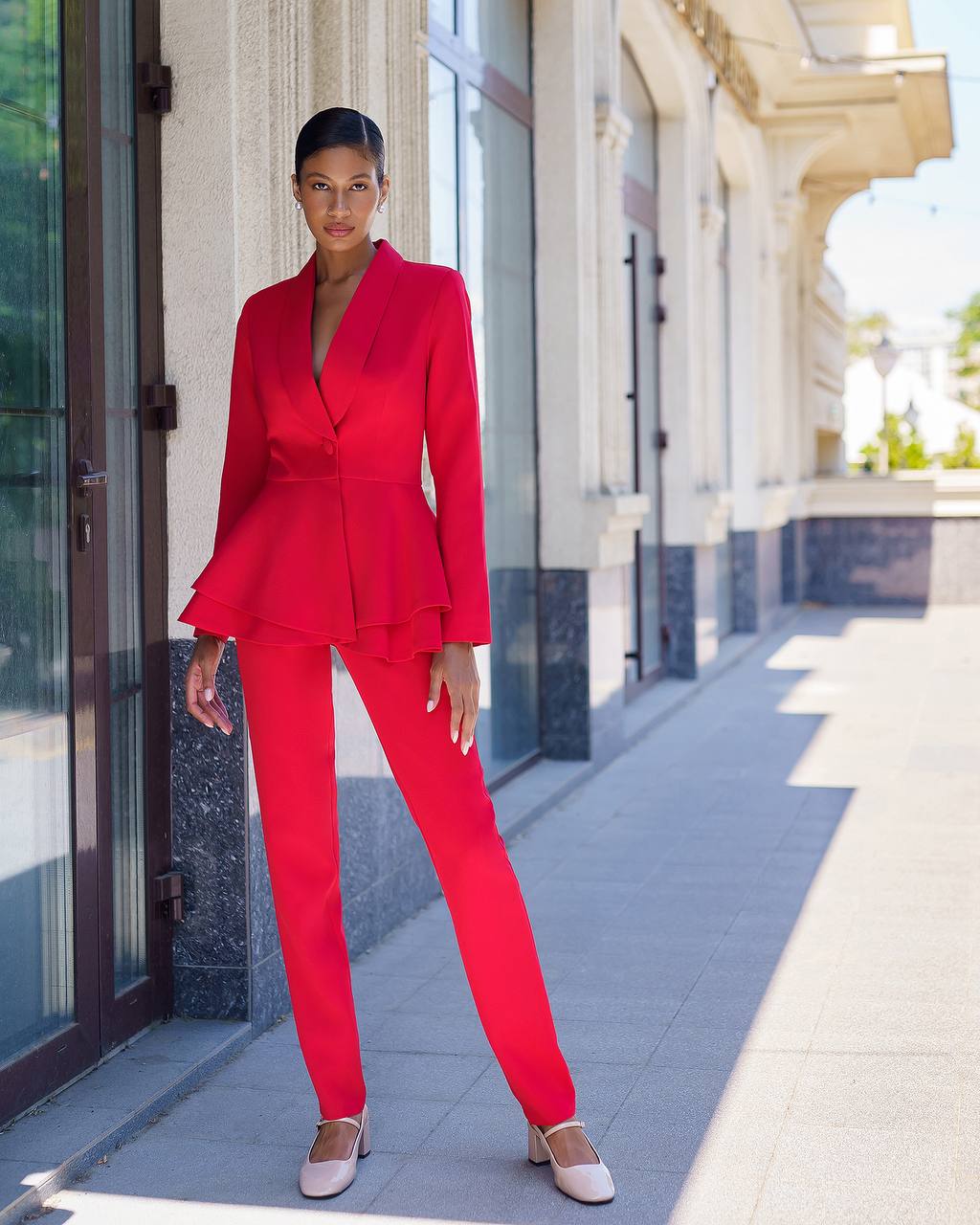 Woman in a red suit standing on a sidewalk with a building in the background