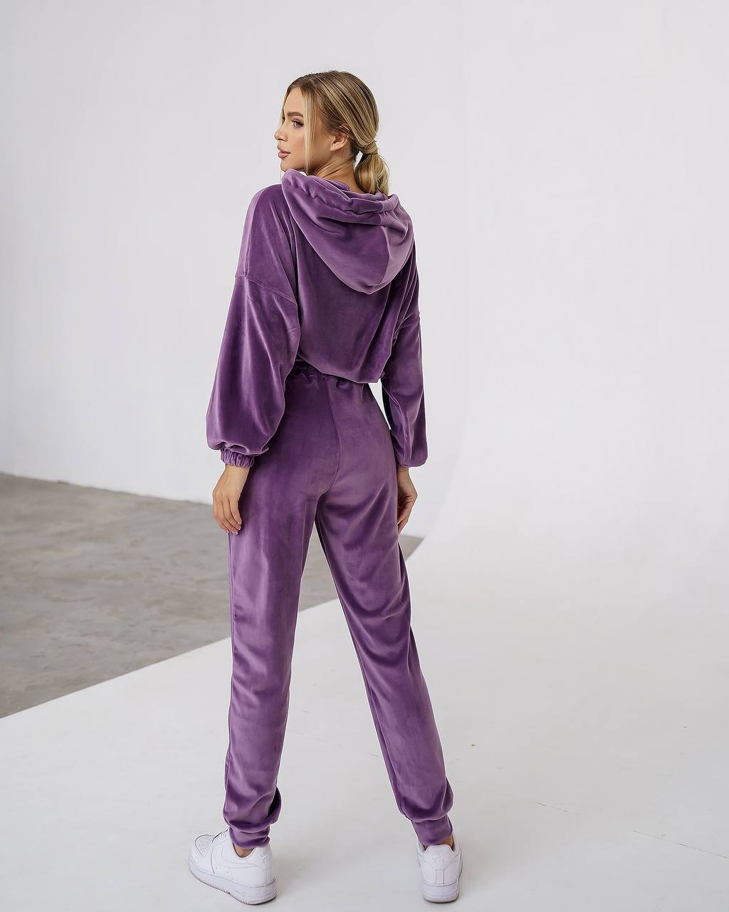 Woman wearing a purple velvet tracksuit on a white background