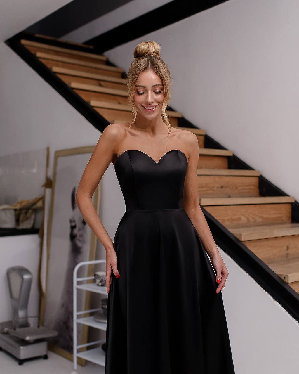 Woman in a black strapless dress standing in front of a staircase.