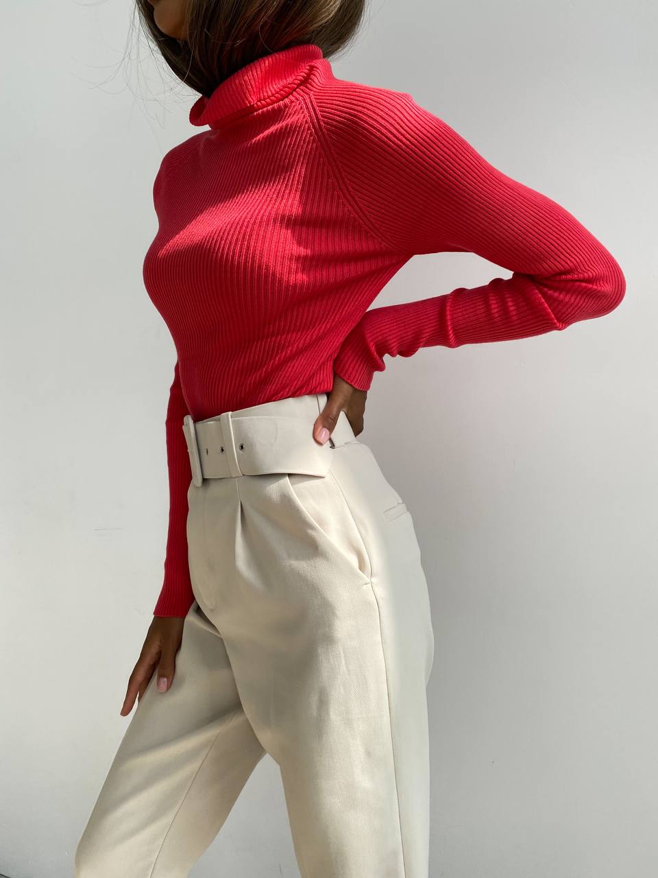 Person wearing a red turtleneck and white pants against a plain background