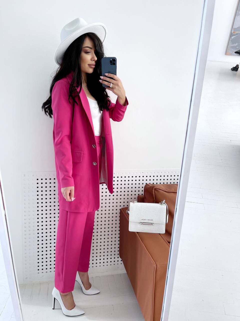Woman taking a mirror selfie wearing a pink suit and white hat.