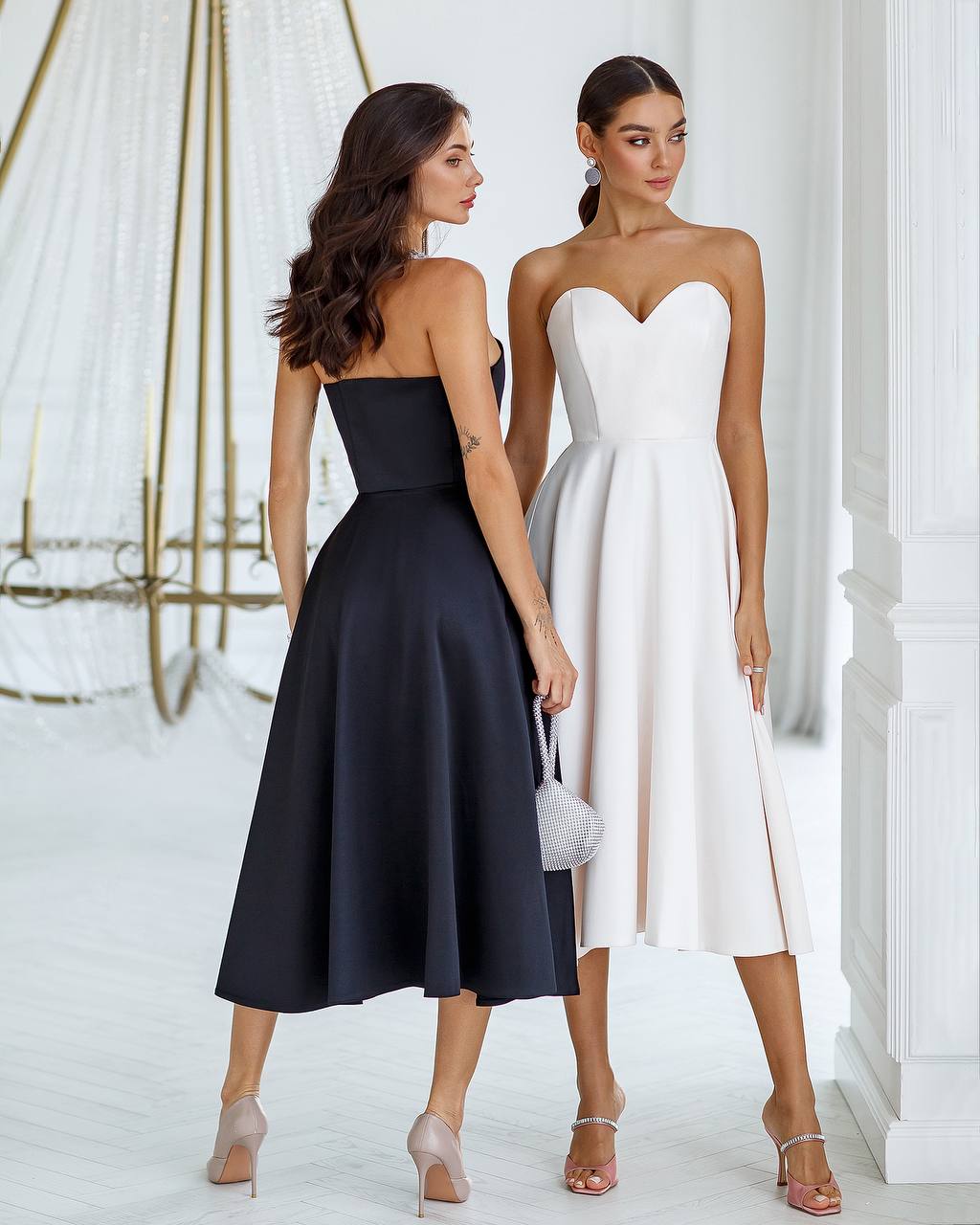 Two women wearing black and white strapless dresses standing side by side.