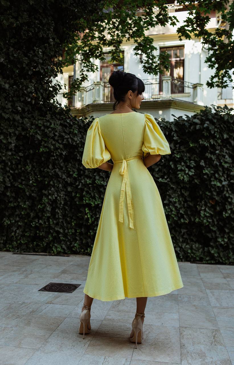 Woman in a yellow dress standing in front of a building with greenery.