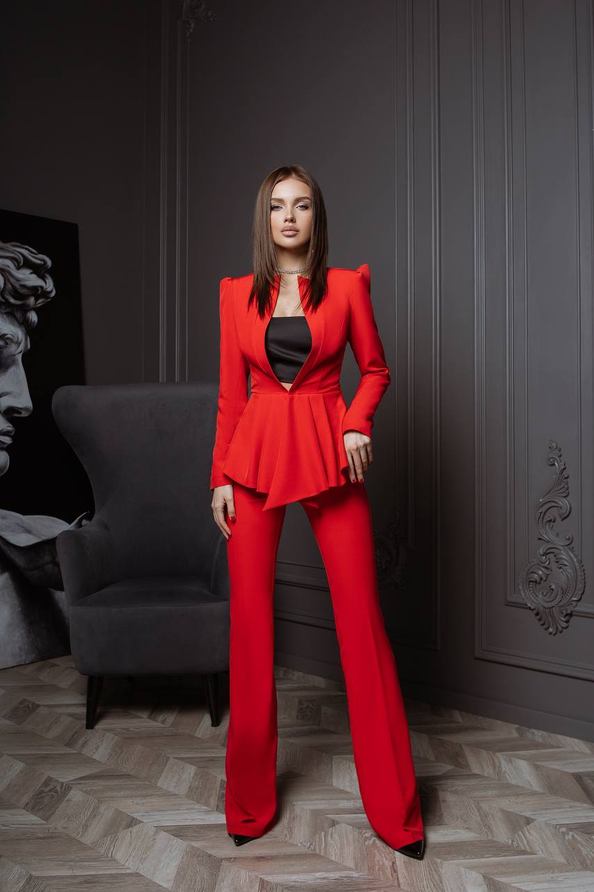Woman in a red suit standing in a room with gray walls and a gray chair.