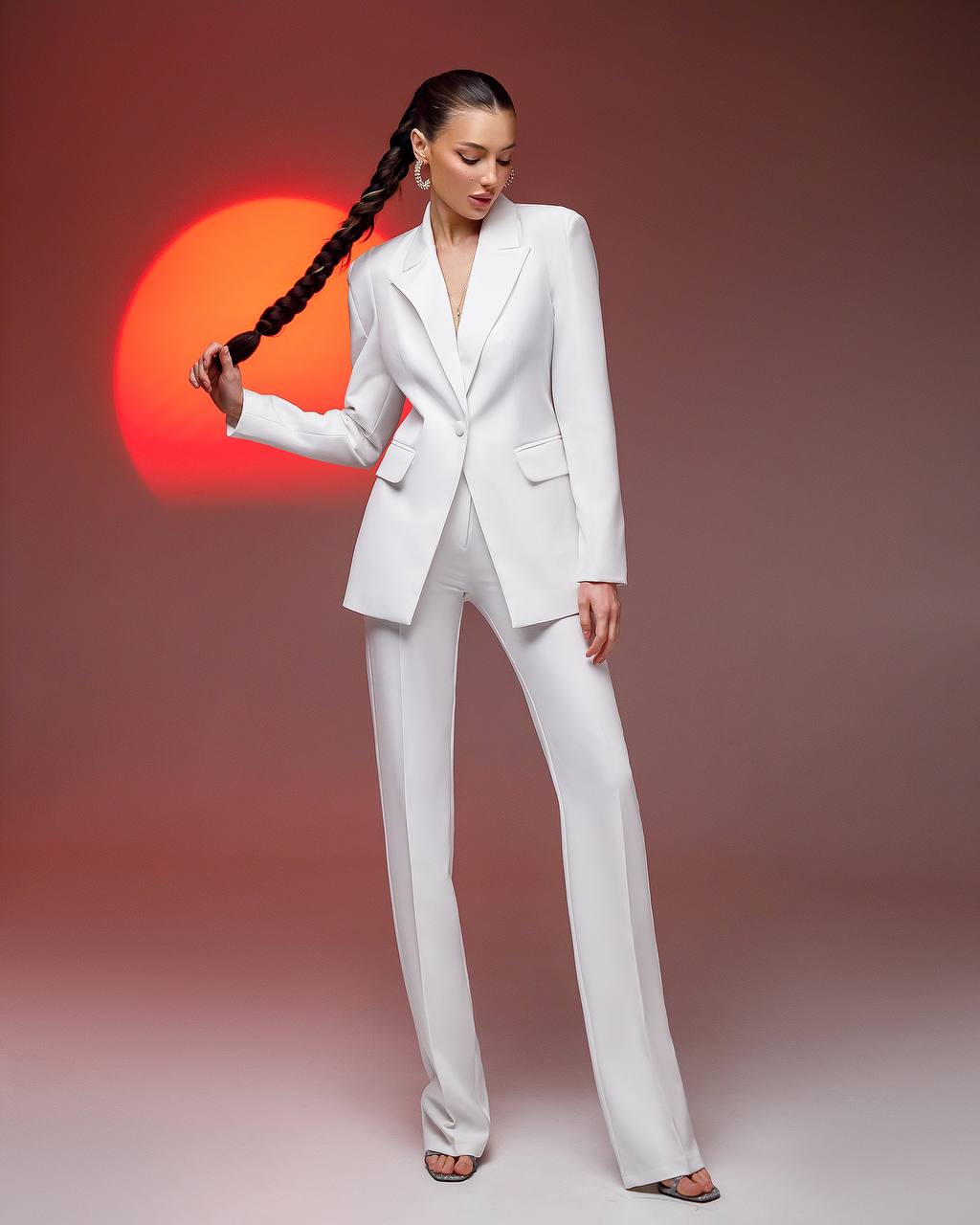 Woman in a white suit standing against a gradient background with a red sun effect.