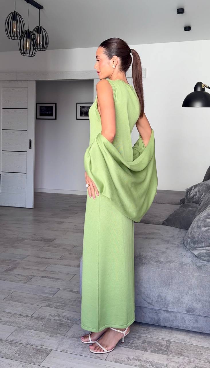 Woman in a green dress standing in a room with a sofa and lamp.