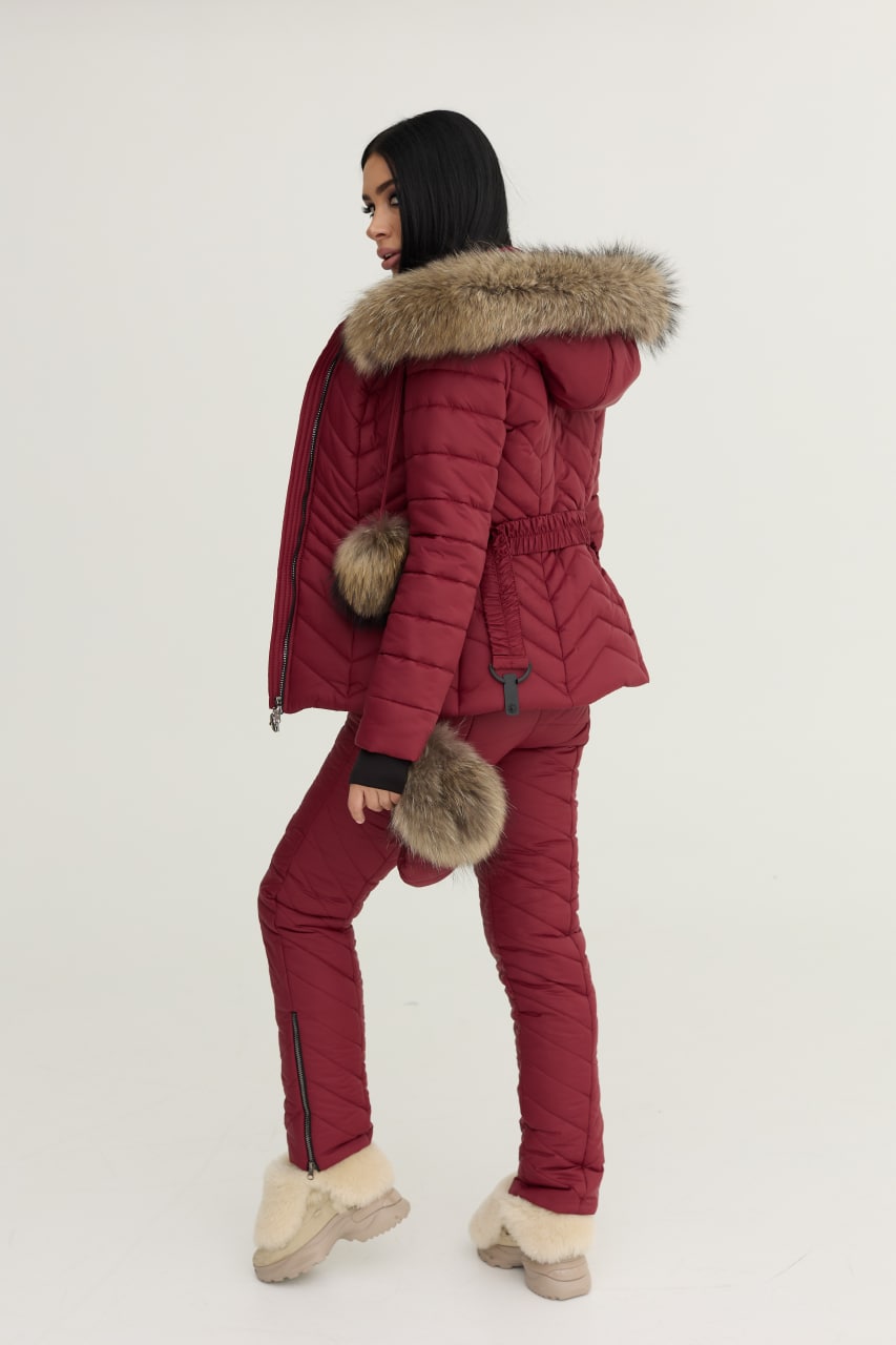 Person wearing a red winter outfit with fur-lined hood and pants on a white background
