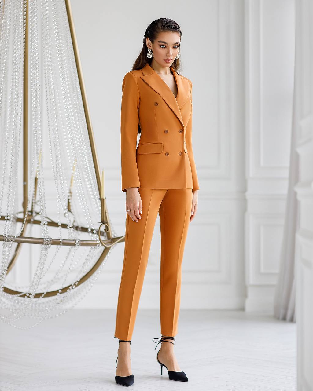Woman wearing a mustard yellow suit standing in a minimalistic room with decorative elements.