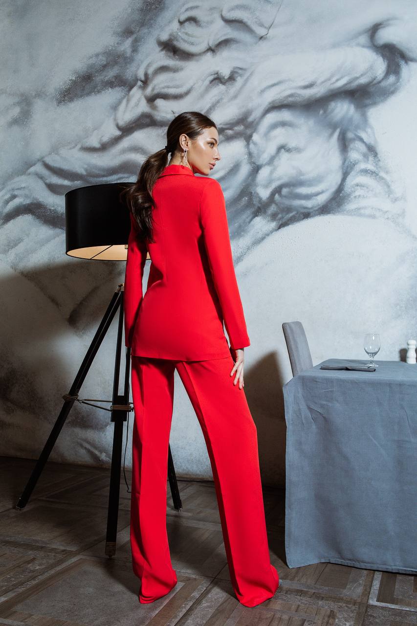 Woman in a red outfit standing in a room with a textured wall and table.