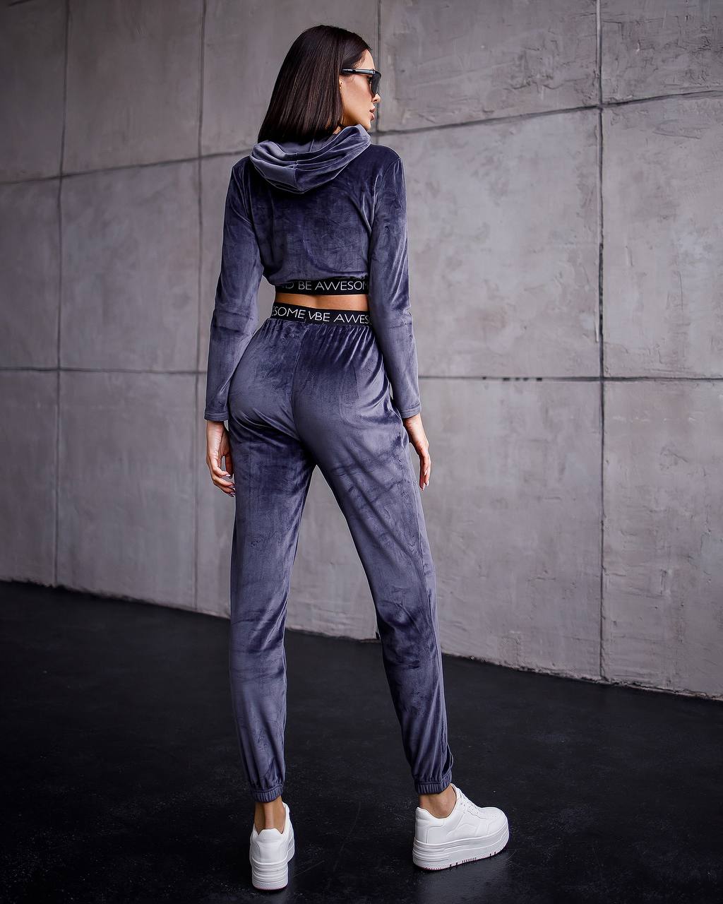 Woman wearing a gray tracksuit with a hood against a concrete wall.