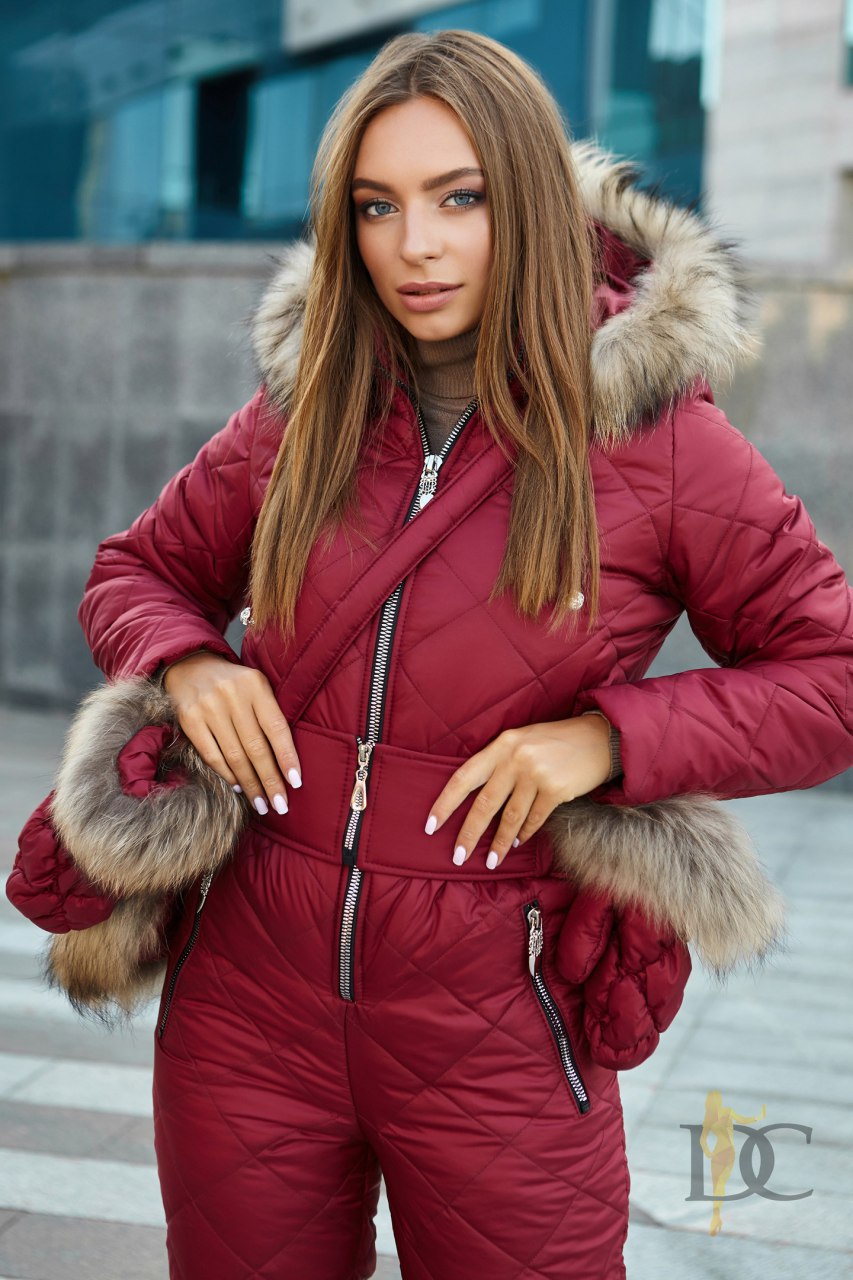 Woman wearing a red puffer jumpsuit with fur trim outdoors.