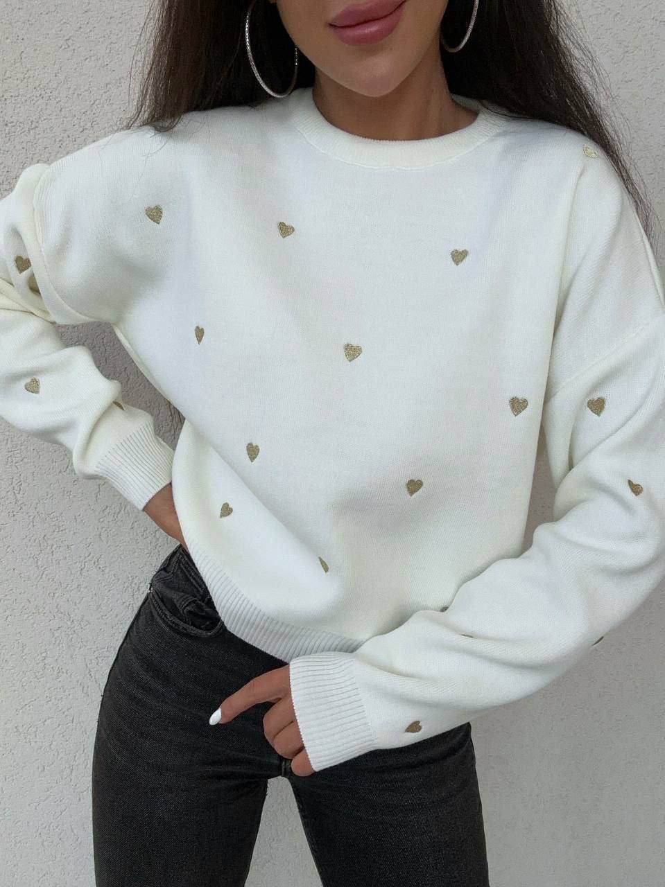 White sweater with gold heart patterns worn by a person against a neutral background