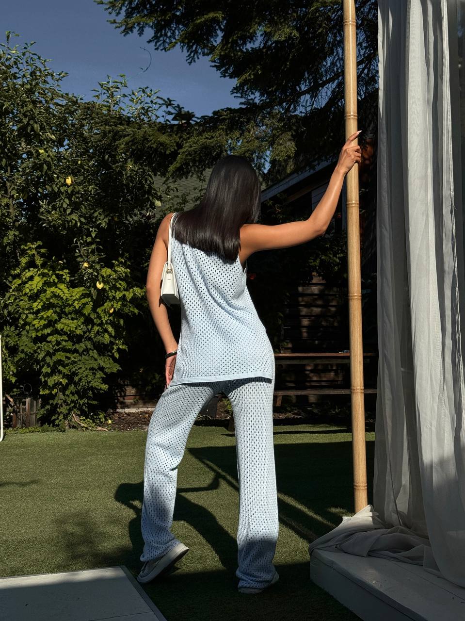 Woman in light blue outfit standing next to a bamboo broom outdoors.