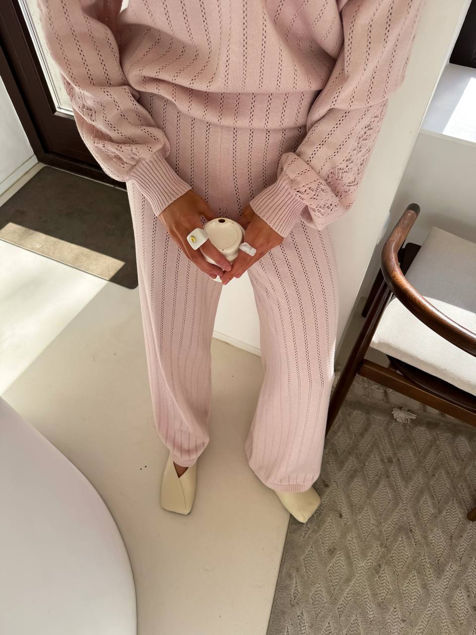 Person wearing a pink knitted outfit holding a small white toy indoors.