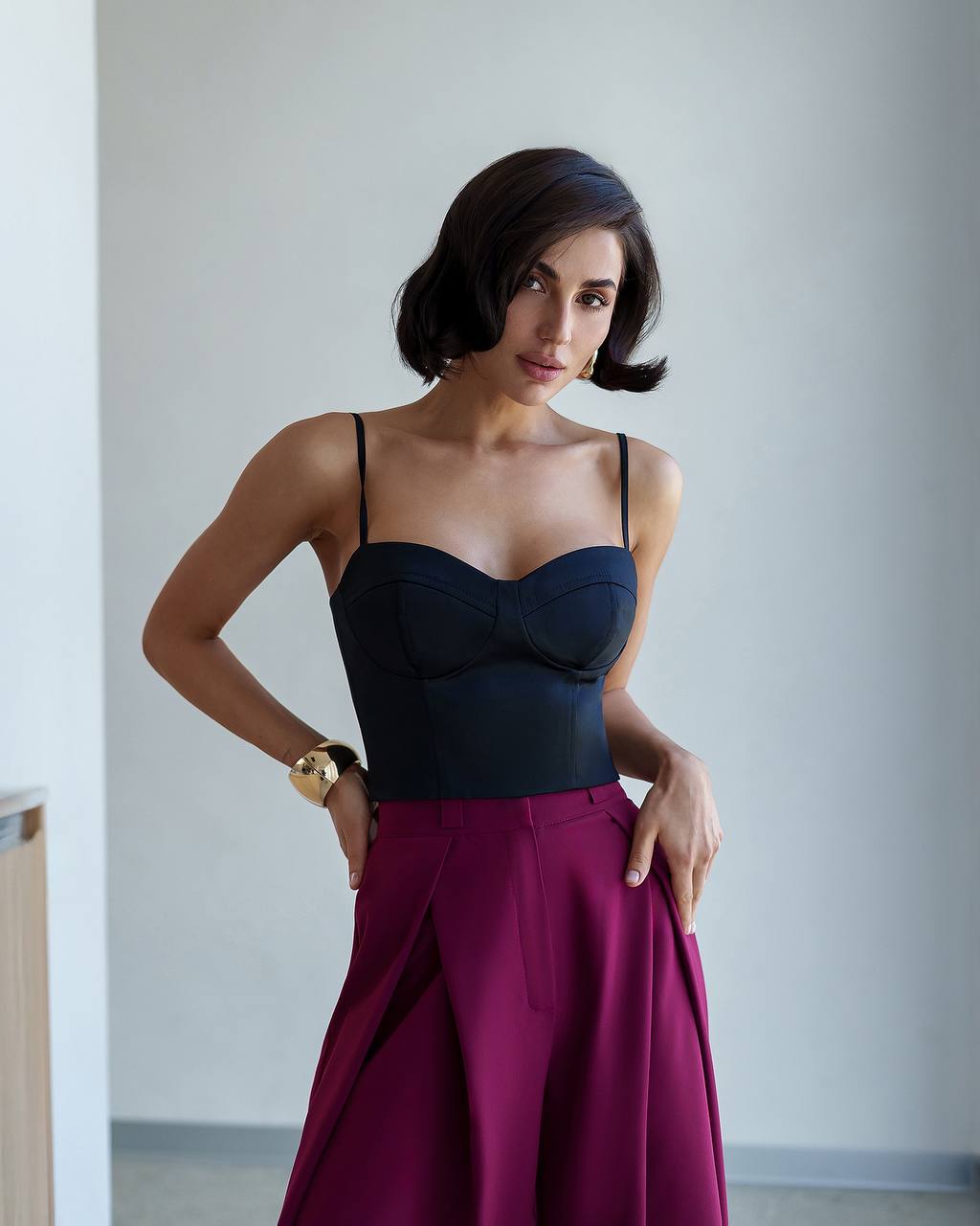 Woman wearing a black top and magenta skirt against a plain background