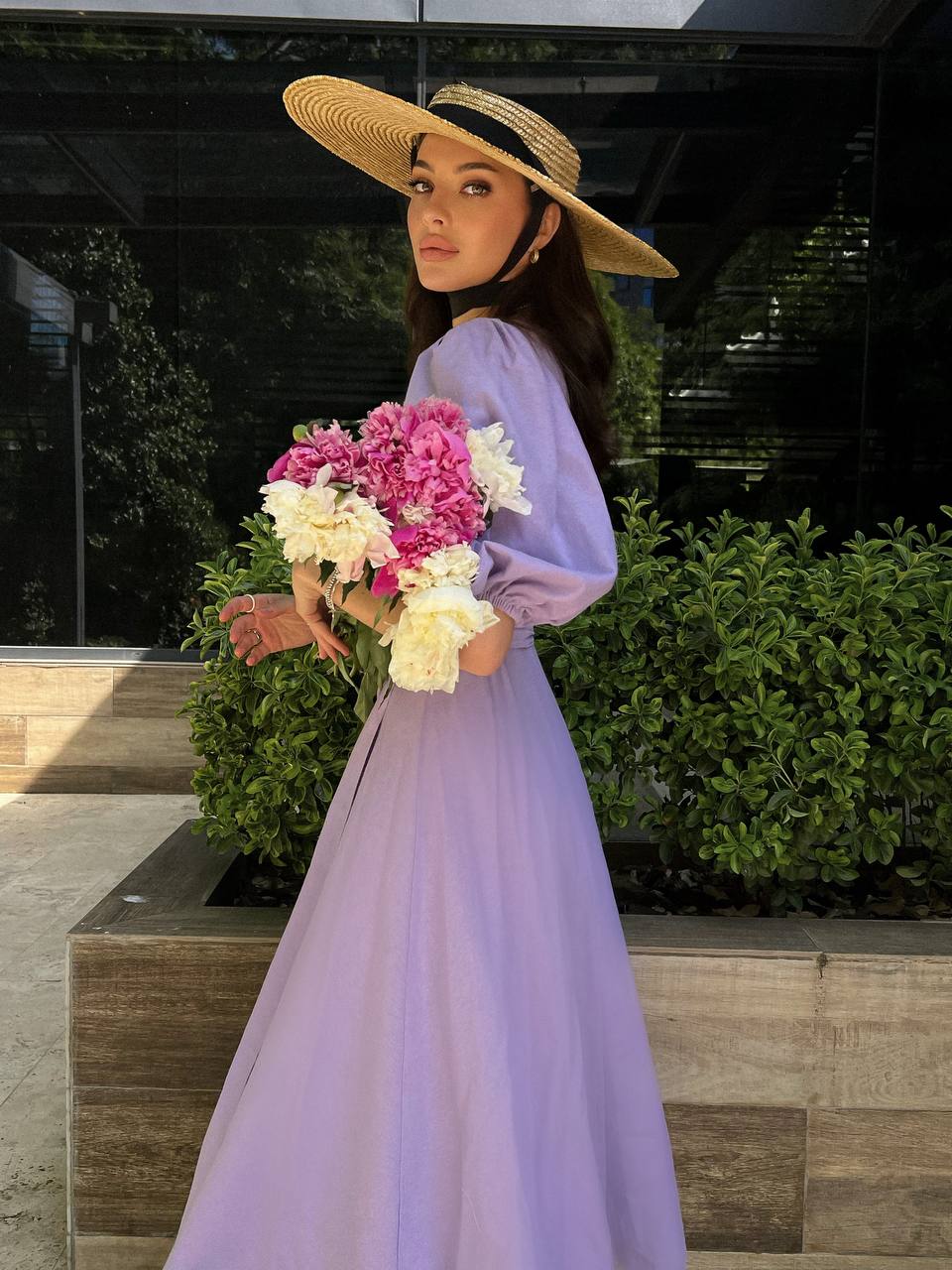 Woman in a long purple dress holding flowers outdoors