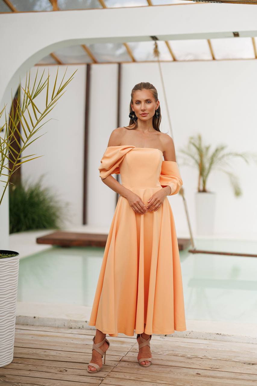 Woman in a peach off-shoulder dress standing in a modern indoor setting with plants.