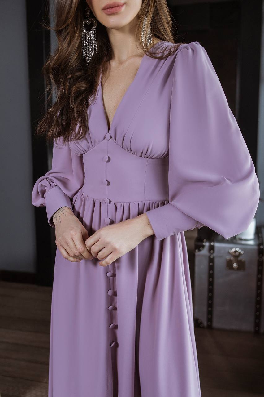 Woman wearing a purple dress with long sleeves in an indoor setting.