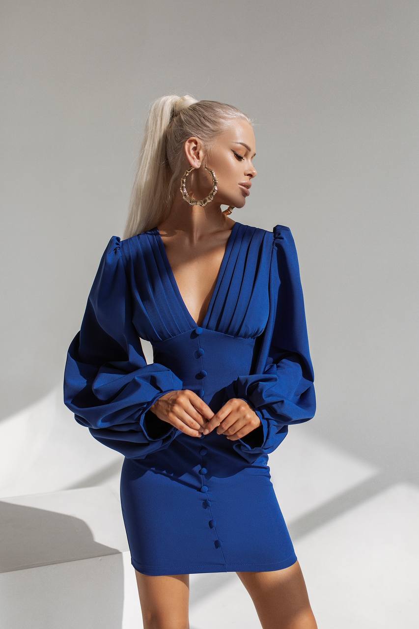 Woman wearing a blue dress with long sleeves against a neutral background