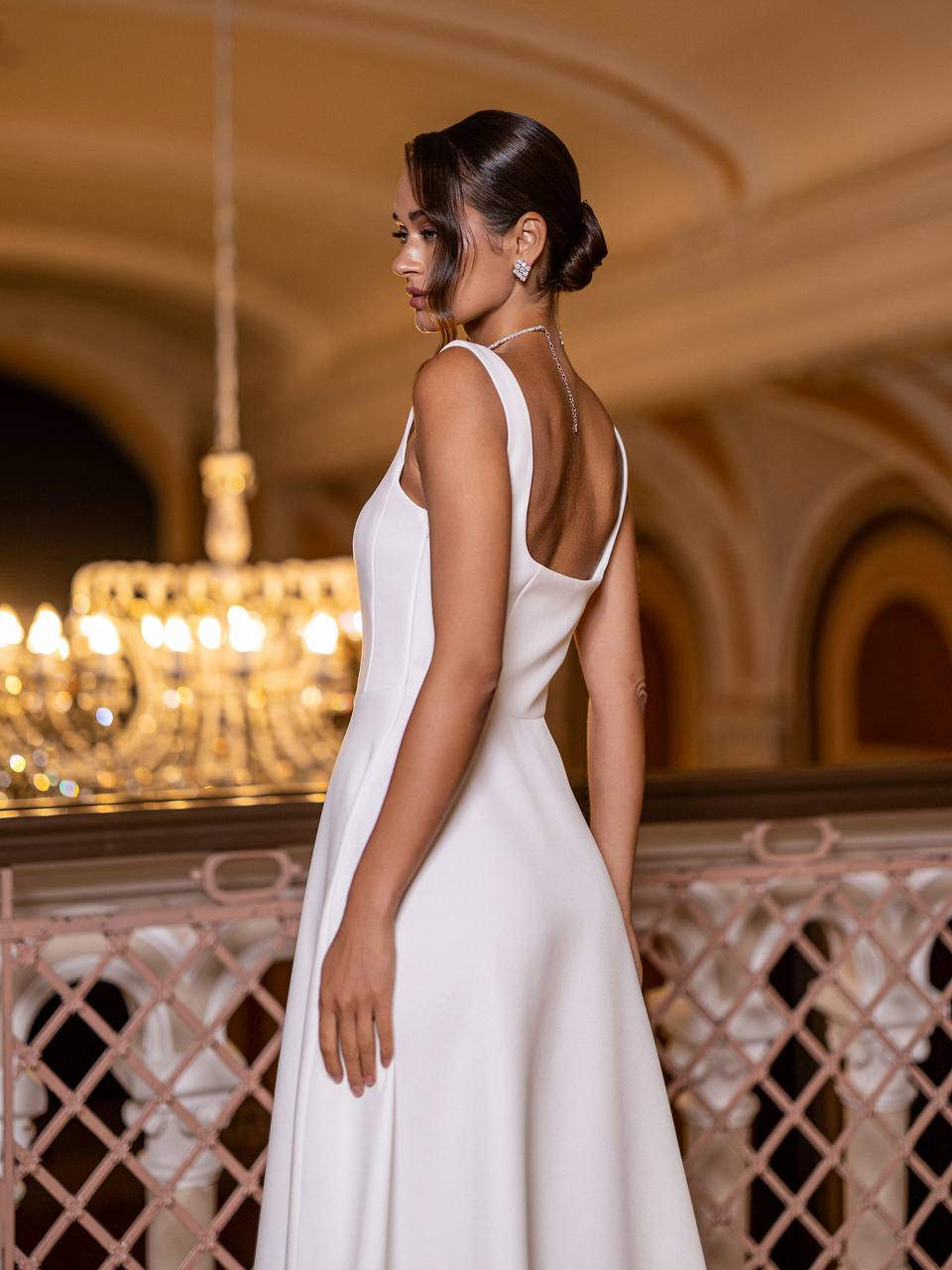 Woman in a white dress standing in an elegant indoor setting with chandeliers.