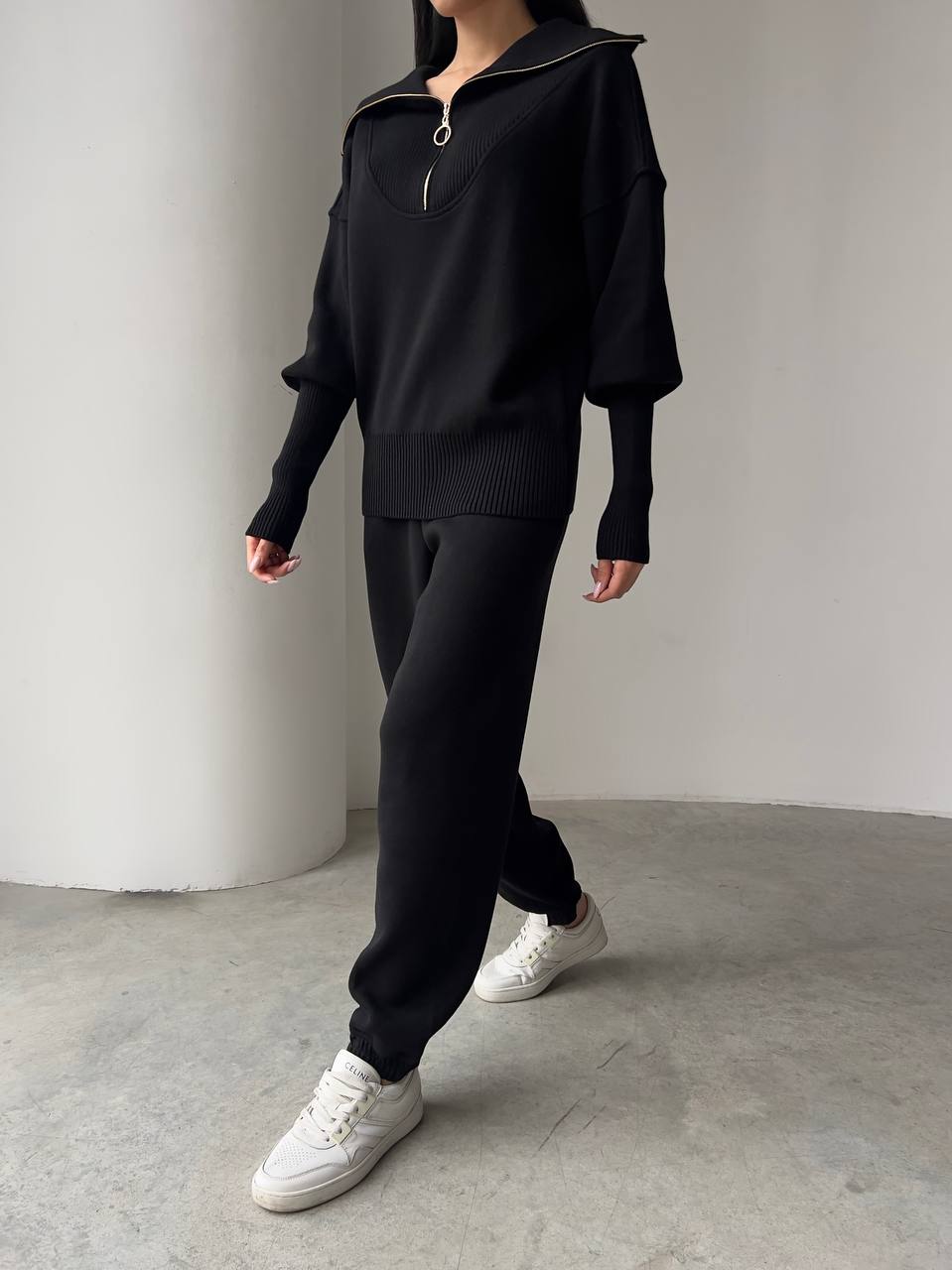 Person wearing a black outfit with white sneakers on a plain background