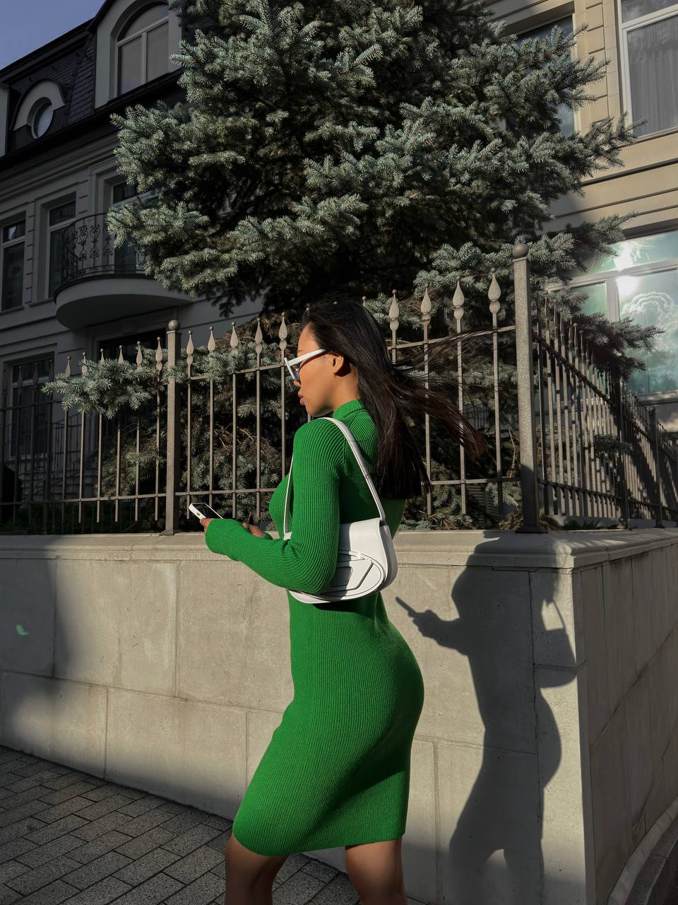Woman in a green dress walking on a sidewalk with a building and tree in the background