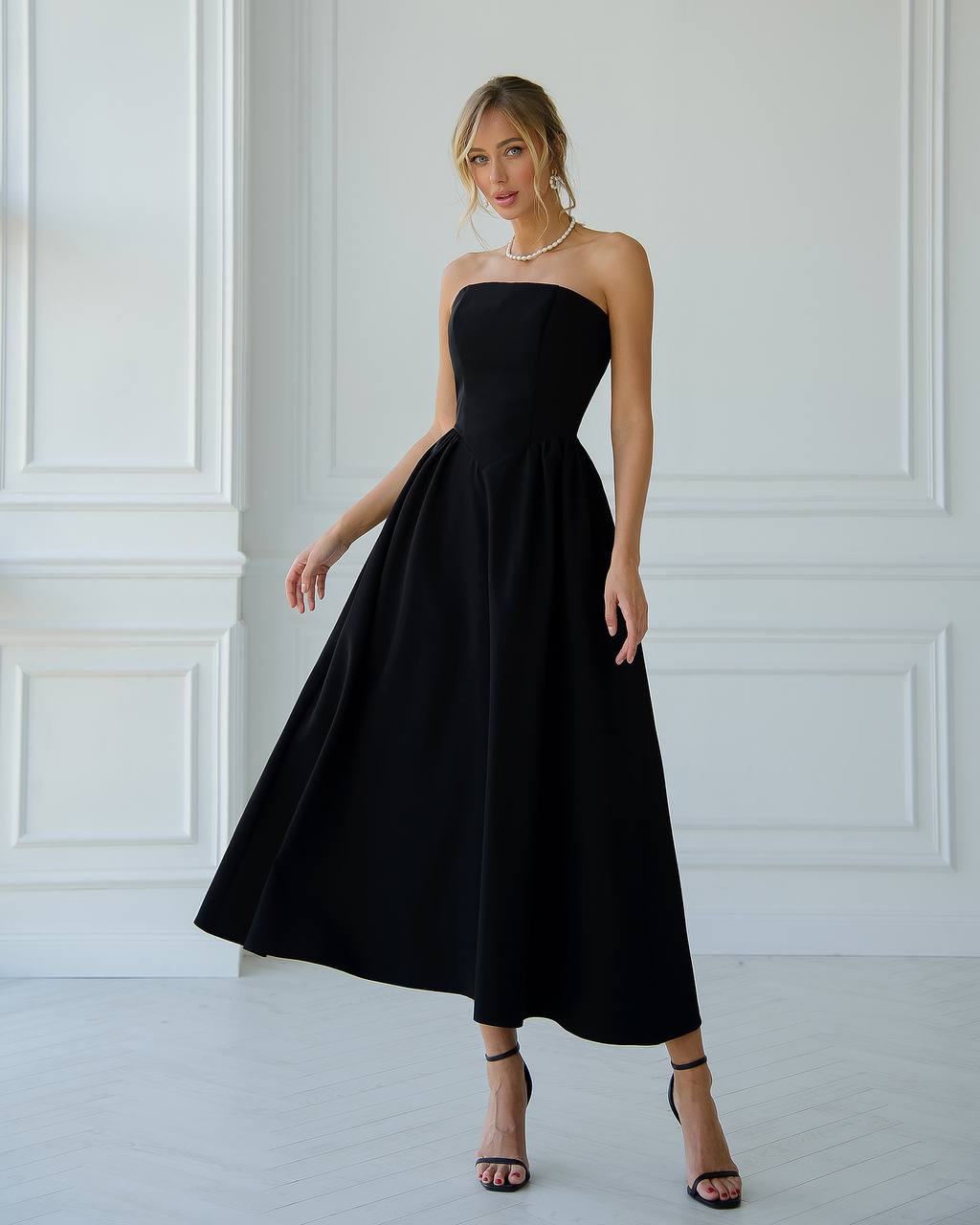 Woman wearing a black strapless dress in a white room