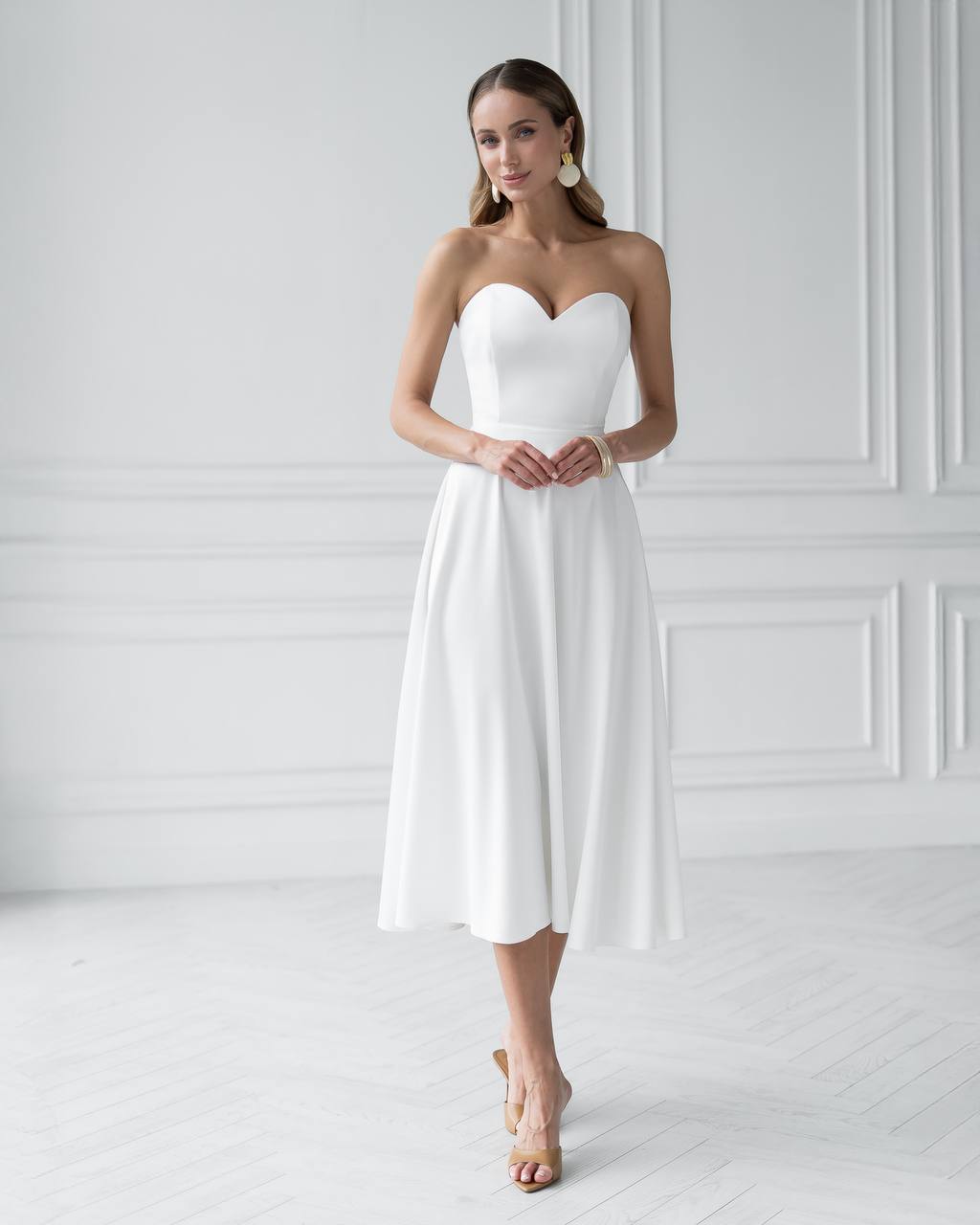 Woman wearing a strapless white dress against a white wall