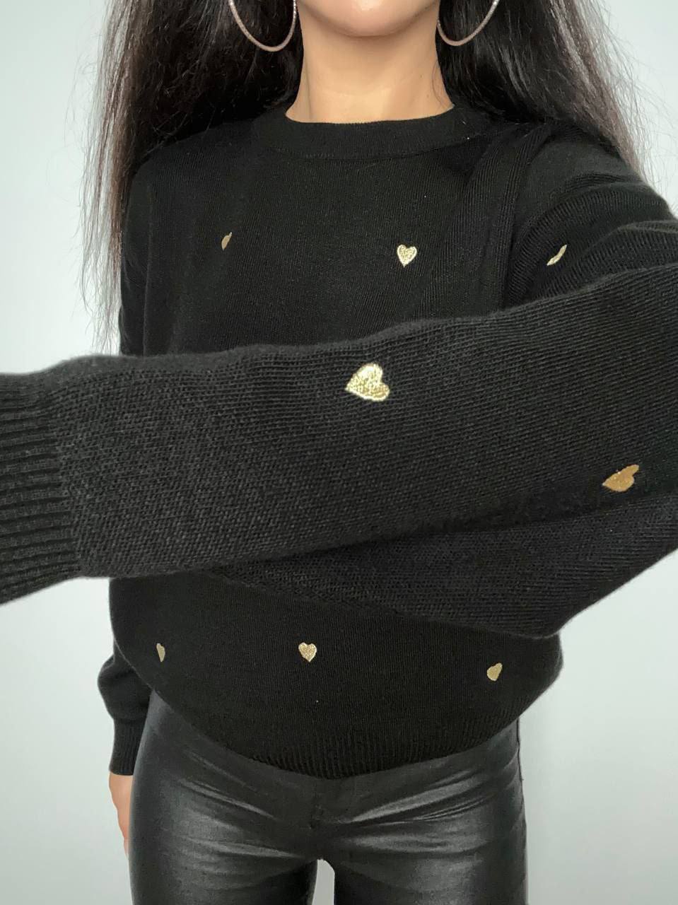 Black sweater with gold heart patterns worn by a person against a plain background