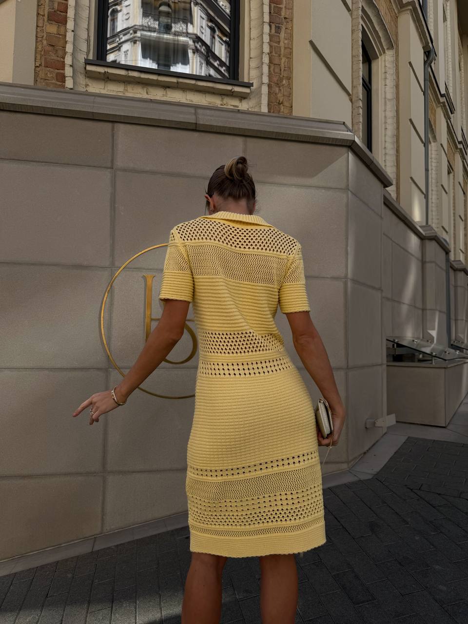 Woman in a yellow dress standing in front of a building with a gold circular design.