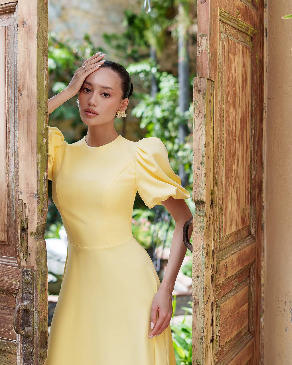 Woman in a yellow dress standing in a doorway with greenery outside