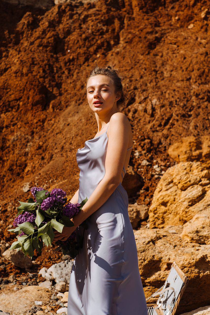 Woman in a gray dress holding a bouquet of flowers against a rocky background