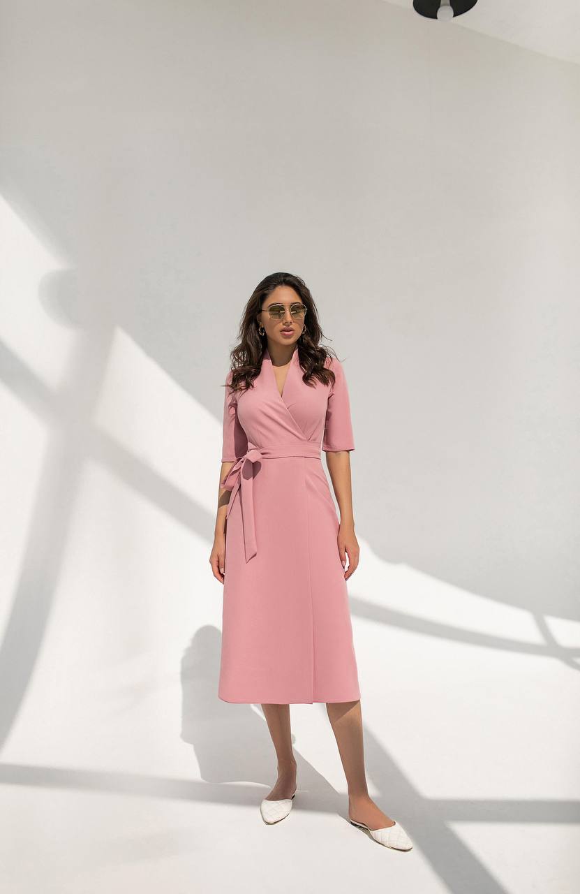 Woman wearing a pink dress standing in a well-lit room with white walls.