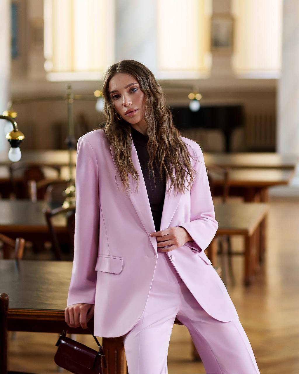 Woman in a pink suit standing in an indoor setting with blurred background