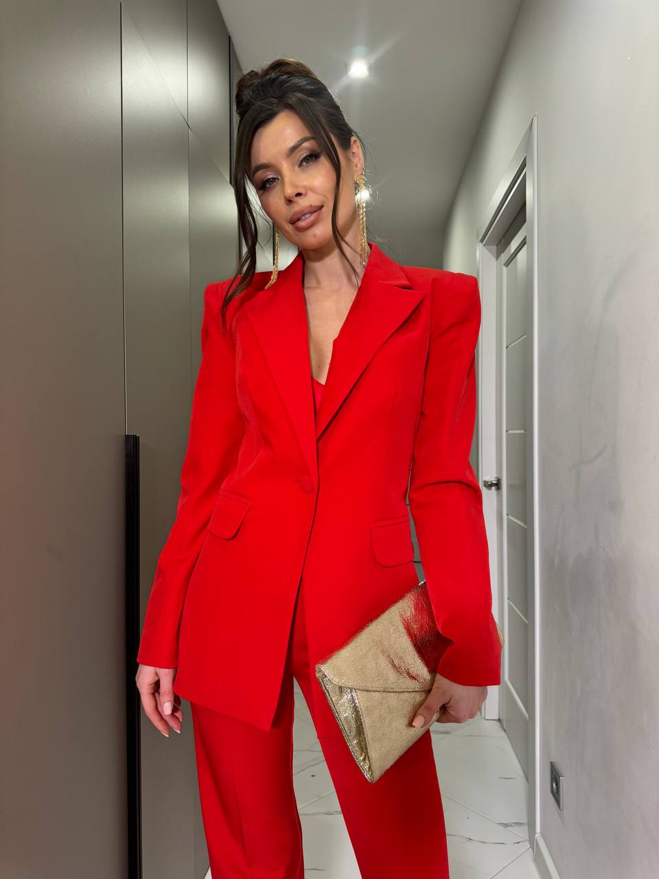 Person wearing a red suit holding a gold clutch in an indoor setting.