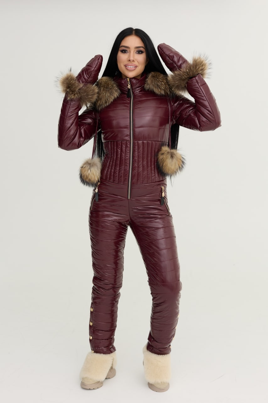 Person wearing a maroon puffer jumpsuit with fur-lined hood and cuffs on a white background