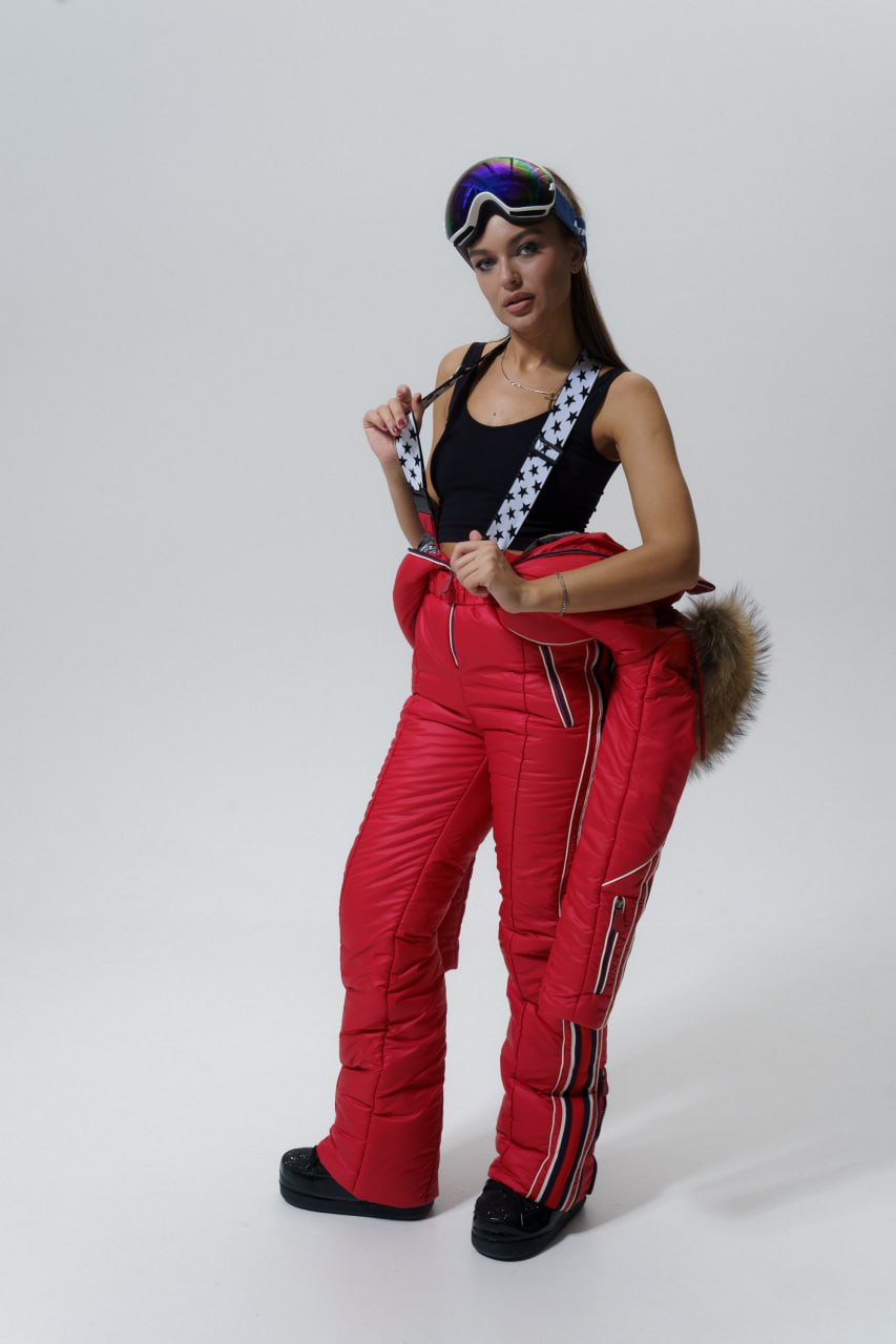 Person wearing red ski pants with a black top and colorful goggles on a white background